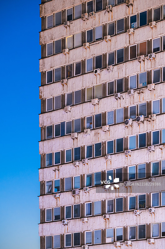 高层建筑的立面，窗户成排，空调外机形成重复的几何图案，在蓝天下营造出抽象、富有纹理的城市建筑景观图片素材