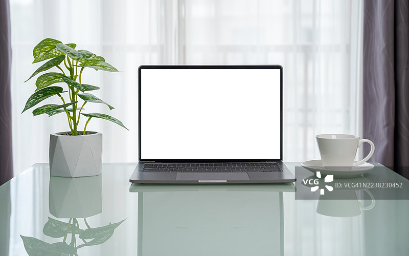 简约办公室内的木质工作桌上放着笔记本电脑、咖啡杯和盆栽植物，笔记本电脑的屏幕是白色的空白。这是一个在家里的工作场所，桌上放着一台笔记本电脑。图片素材