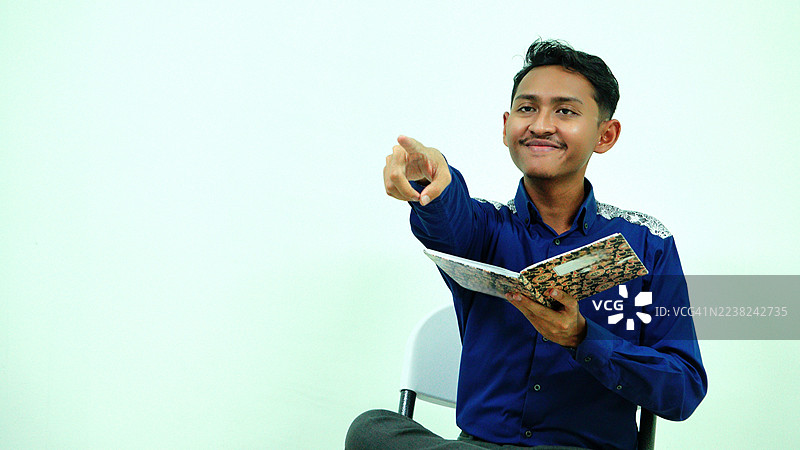 在商务会议中，一位年轻男子手持书籍，手指指向观众图片素材