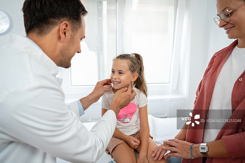 儿科医生在明亮的诊所里为一位开心的女孩病人进行检查，她身旁有支持她的母亲。图片素材