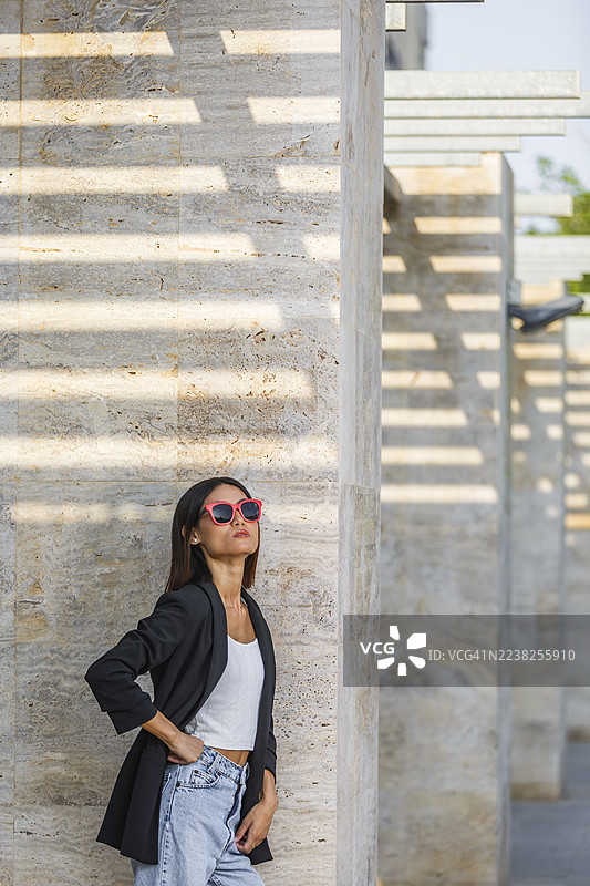 身着太阳镜和休闲装的女性在西班牙的纹理石墙前摆姿势。图片素材