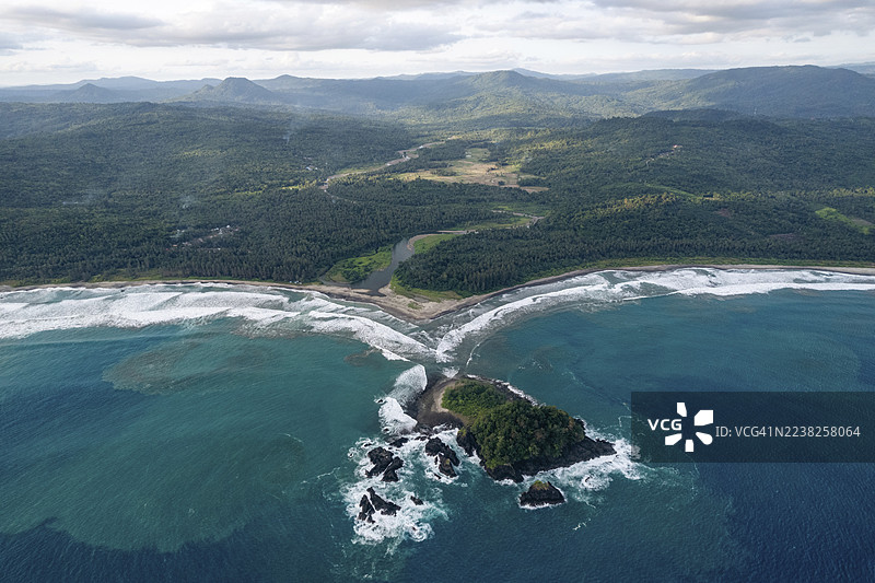 海岸线鸟瞰图，有海浪、茂密的绿色山丘和一个小岛。印度尼西亚北苏门答腊省南尼亚斯。图片素材