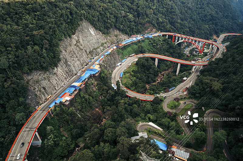 航拍蜿蜒的山路，周围是郁郁葱葱的绿林和鲜红的桥梁。位于印度尼西亚西苏门答腊省哈劳的九曲湾（Kelok 9）。图片素材