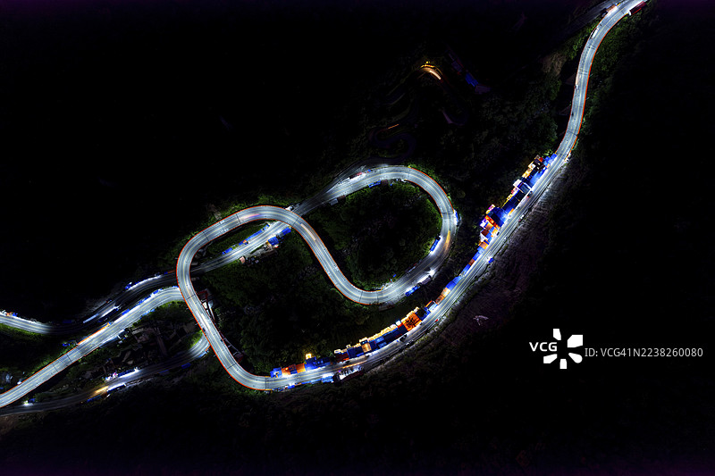 夜景航拍，蜿蜒的道路上有五彩斑斓的车灯，置身于黑暗的风景中。位于印度尼西亚西苏门答腊省哈劳的九曲十八弯（Kelok 9）。图片素材