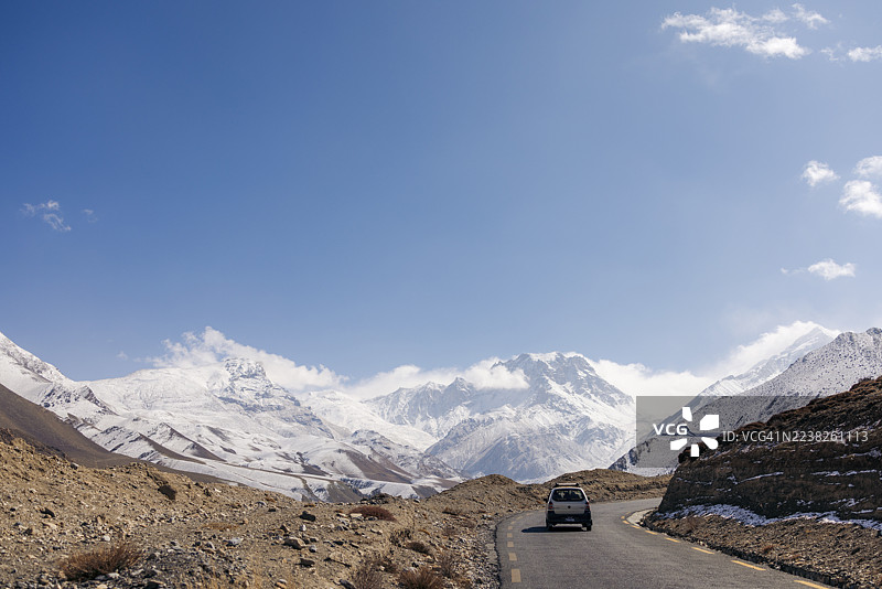一辆汽车在清澈的蓝天下，行驶在穿越雪山风景的蜿蜒道路上。F042公路，安纳布尔纳，马斯塘县，甘达基省，尼泊尔图片素材