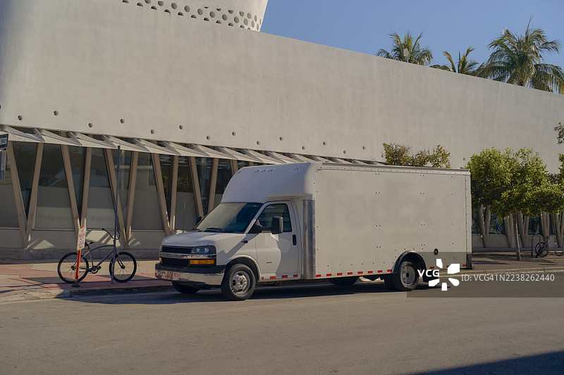 一辆白色的送货货车停在阳光明媚的街道旁，旁边是一栋现代建筑和自行车。佛罗里达州迈阿密，美国图片素材