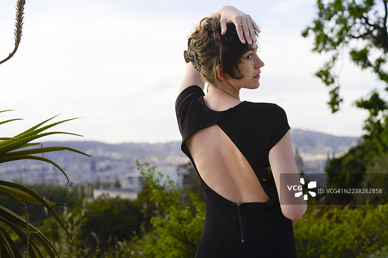 身穿镂空黑色连衣裙的女子在户外摆姿势，背景是城市天际线和树木。图片素材