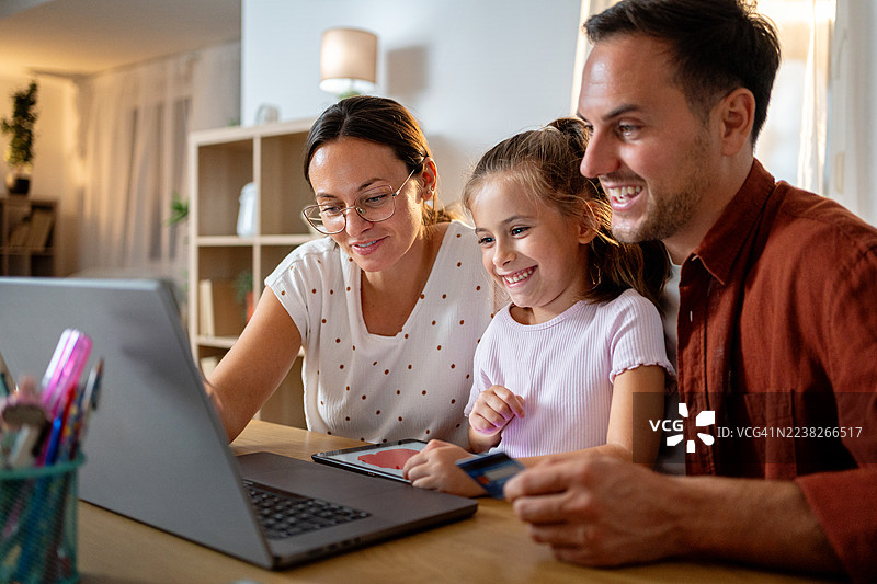 快乐的一家在家里使用笔记本电脑，用信用卡进行在线购物。图片素材