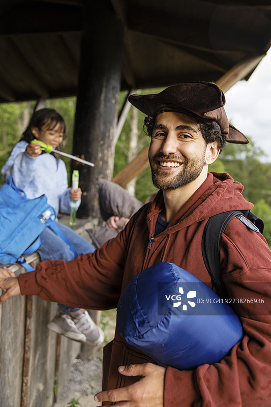 夏令营中，一位戴着三角帽、面带微笑的男性向导，手中拿着睡袋的肖像照。图片素材