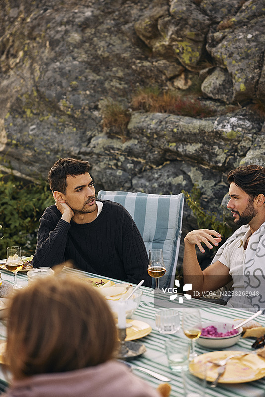 俯视角度拍摄，一名男子坐在餐桌旁，在岩石山丘附近与男性朋友交谈图片素材