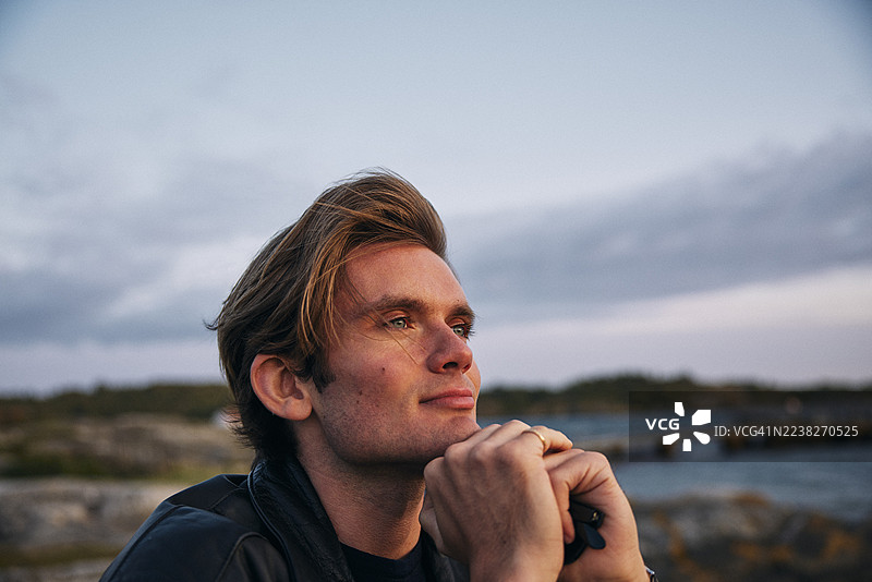 沉思的年轻男子，手托下巴，望向远方图片素材