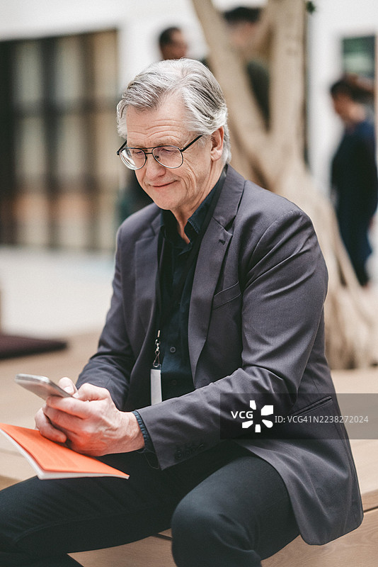 一位年长的男性商业专家在国会中心坐着用智能手机图片素材
