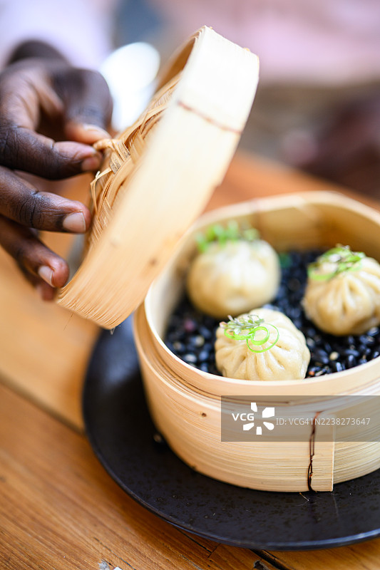 特写：打开竹蒸笼，里面是撒有新鲜微型蔬菜的精致点心饺子图片素材