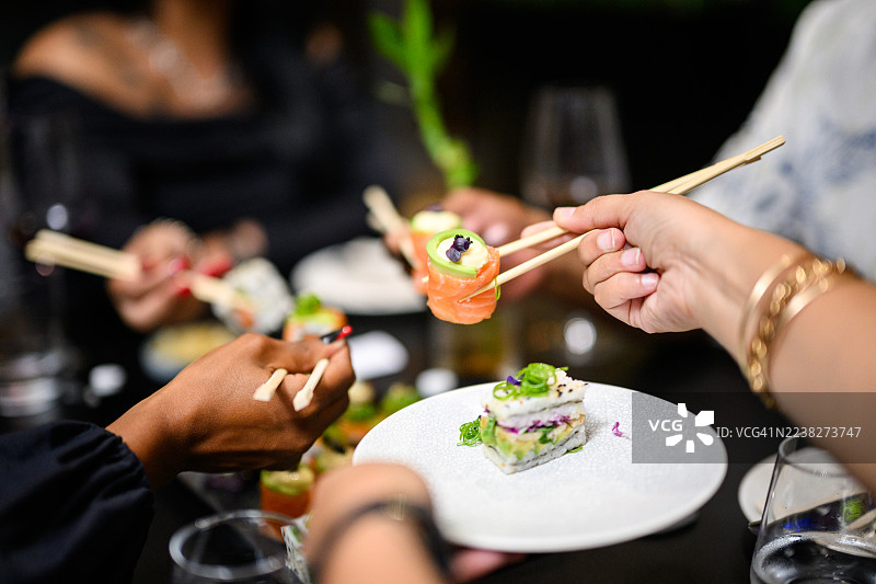 特写镜头，食客们用筷子从共享拼盘中挑选三文鱼玫瑰和牛油果寿司图片素材