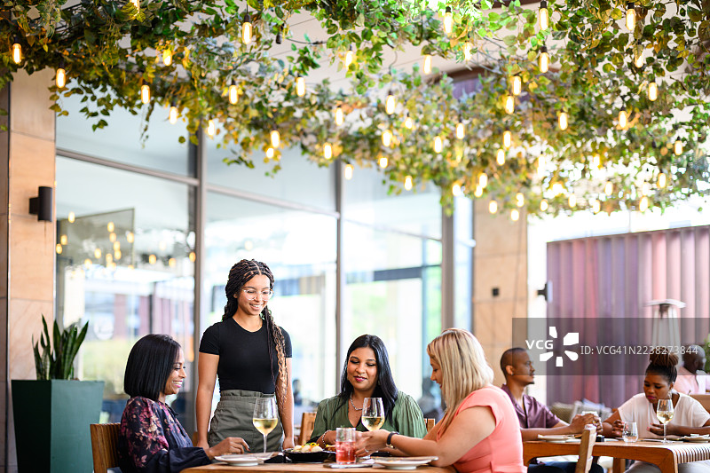 俯瞰视角，户外餐厅露台上，女服务员正在为顾客提供服务，背景是郁郁葱葱的绿植和悬挂的灯饰图片素材