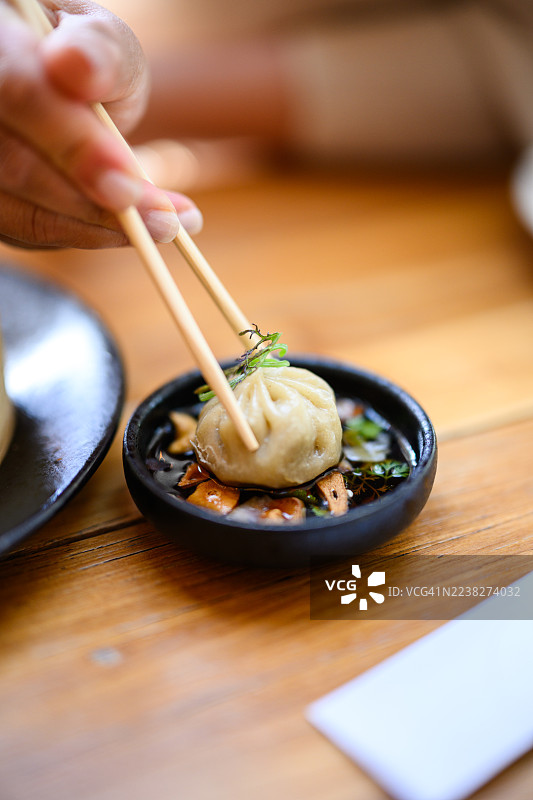 特写：用筷子夹着点心饺子，上方是装有蘑菇和香草的蘸料碗图片素材