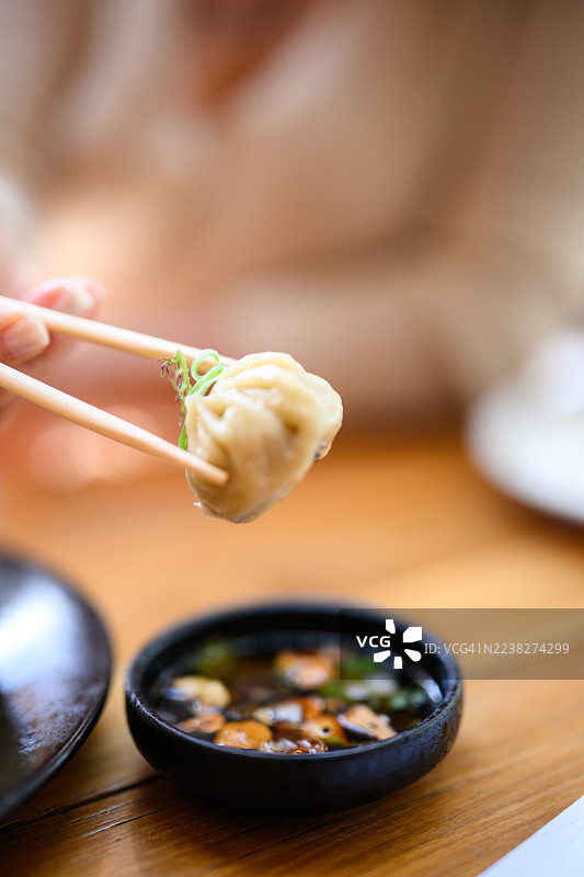 特写：筷子夹着点心饺子，饺子上方是盛有蘑菇和香草的蘸料碗图片素材