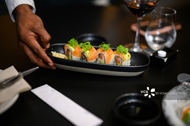 长黑色盘子里盛放着三文鱼玫瑰，饰以牛油果微型蔬菜，置于餐厅桌上，特写镜头图片素材