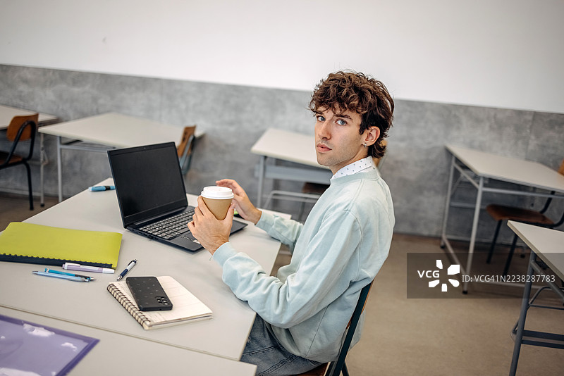 年轻男子在大学学习，手中拿着咖啡杯的肖像图片素材
