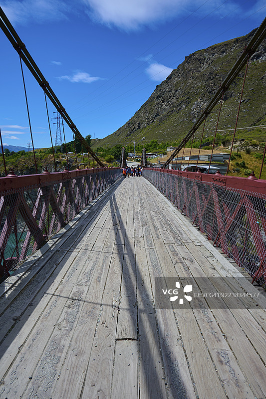 带有红色栏杆的木制人行桥,有阴影和山峦背景,位于新西兰南岛奥塔哥皇后镇的卡瓦劳峡谷大桥,卡瓦劳河。图片素材