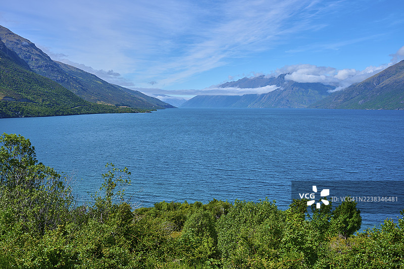 新西兰南岛奥塔哥皇后镇湖区瓦卡蒂普湖漂流湾,群山环绕下的湖泊与蓝天,背景是连绵的山峦。 (View of a lake framed by mountains and a blue sky, Drift Bay, Lake Wakatipu, Queenstown-Lakes District, Otago, South Island, New Zealand)图片素材
