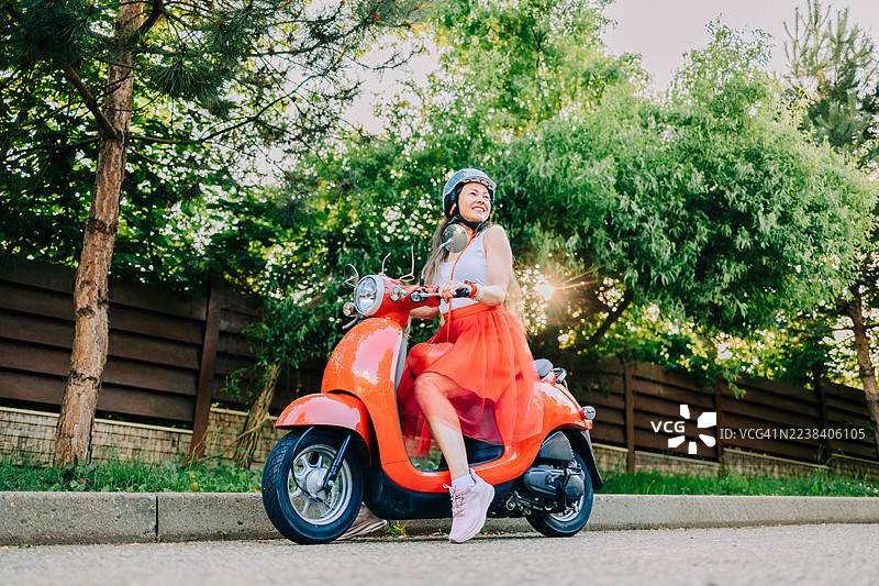 年轻女子在夏日街头骑红色踏板车享受乐趣图片素材