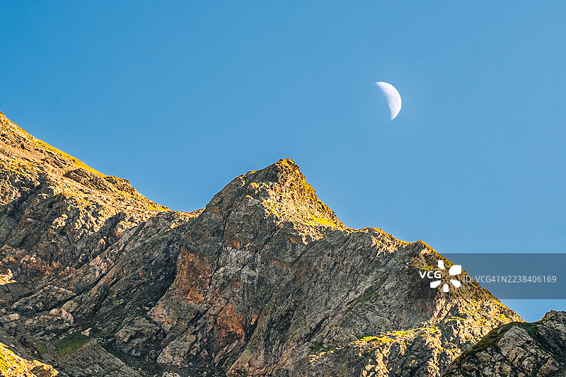 晴朗的蓝天下，月亮和阳光照射的山峰图片素材