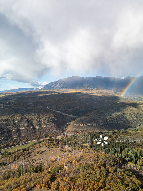 风景优美的空中视角，展现了秋季生机勃勃的山脉、森林和彩虹，天空布满云彩。图片素材