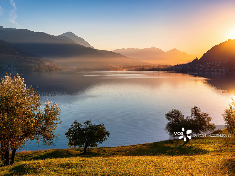 日落时分，宁静的湖泊、山峦和树木构成一幅宁静迷人的风景画，瑞士卢加诺。图片素材