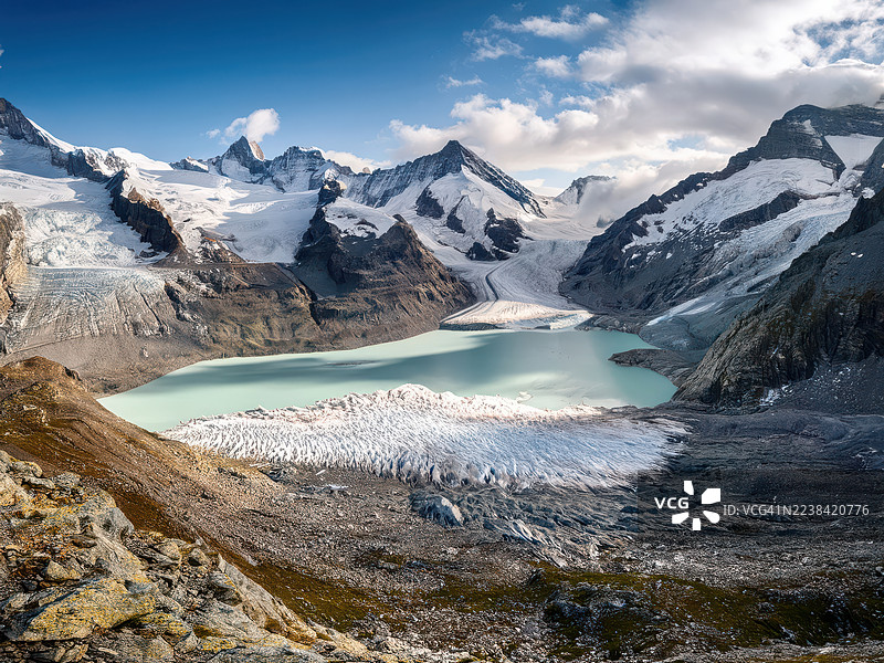 瑞士恩格尔贝格铁力士峰，白雪皑皑的山峰环绕着冰川湖，天空湛蓝，点缀着几朵云彩，令人惊叹的航拍景象。图片素材