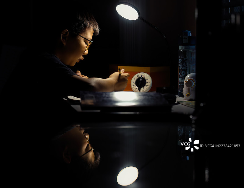 昏暗房间里，一个人在明亮台灯下专心学习或工作图片素材