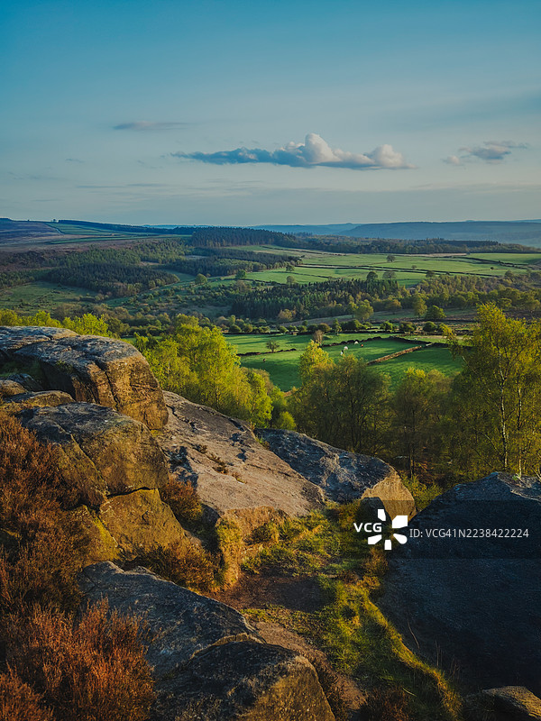蓝天下，广阔的绿色景观，有森林和田野，前景中有巨大的岩石构造，戏剧性的风景。图片素材