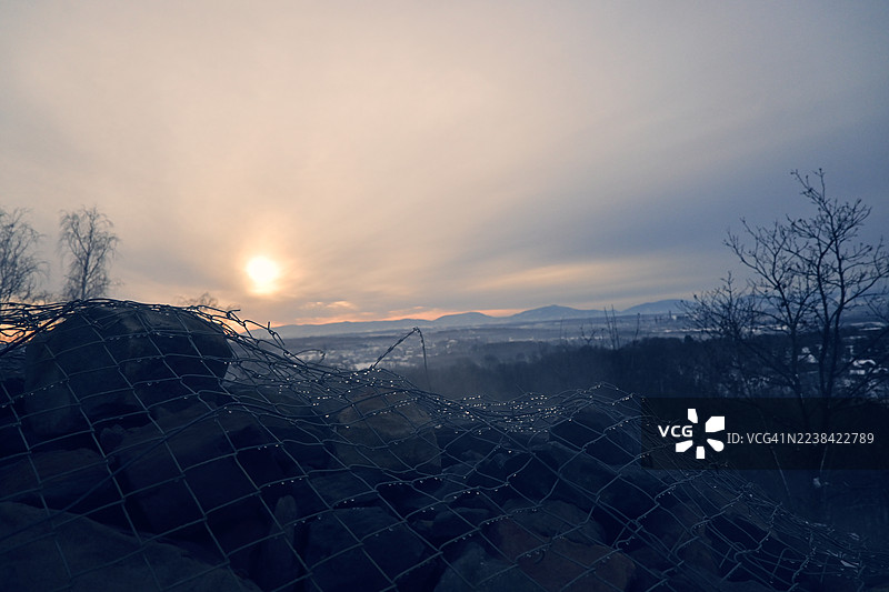 日落时分，雪山在壮丽的天空下构成风景，前景中有栅栏和光秃的树木。图片素材