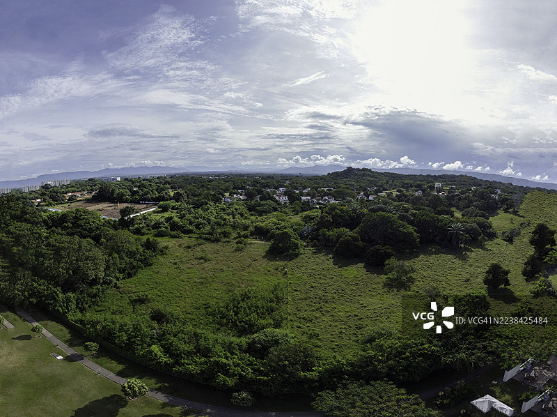 俯瞰郁郁葱葱的绿色景观，有树木和远处的建筑，天空多云。图片素材