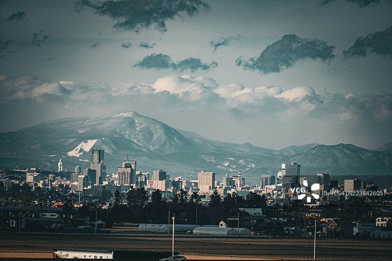 日本仙台，阴云密布的天空下，雪山背景下的现代化城市全景。图片素材