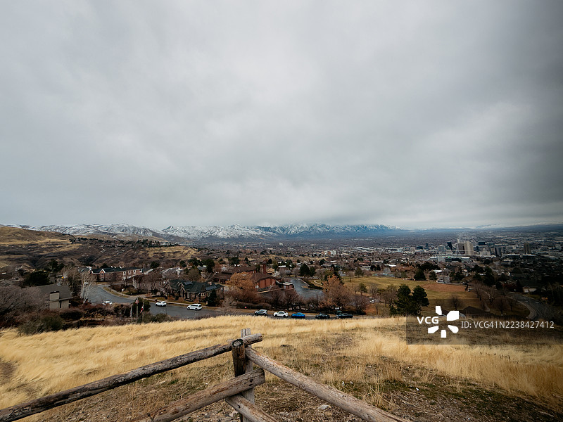 俯瞰广阔的冬季景观，城市坐落在白雪皑皑的山脉下方，天空布满云彩。图片素材