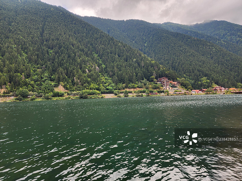 土耳其阿特拉巴扎恩达赫，云层下的青山环绕着宁静的湖泊，远处岸边可见建筑的风景图片素材