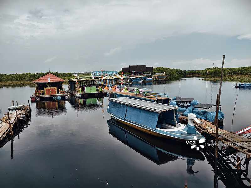 从高处俯瞰，宁静的湖面上泊着几艘船，四周绿意盎然，天空布满云彩。图片素材