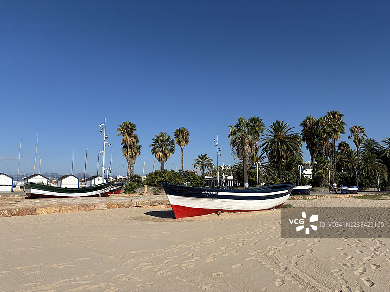 沙滩上的船只，配以棕榈树和湛蓝的天空，营造出宁静的海滨氛围。图片素材