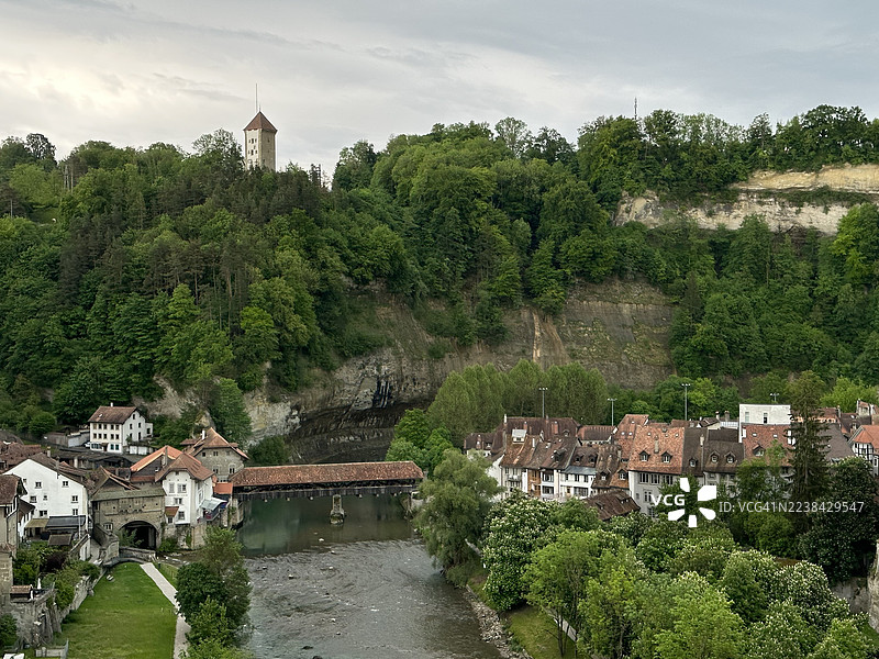 高角度拍摄的河畔历史建筑和茂密绿树，位于一座迷人的欧洲城镇，天空多云，瑞士弗里堡，扎赫林根桥图片素材