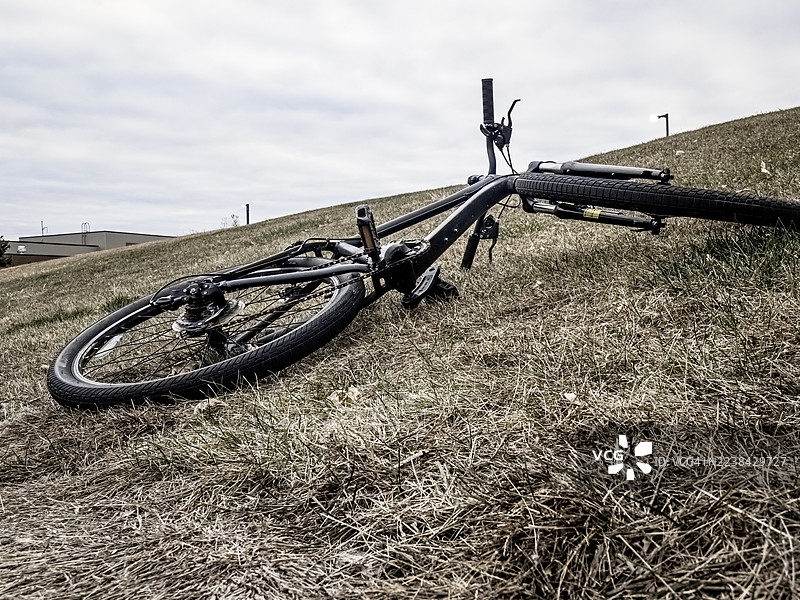 一辆自行车停在多云天空下的草坡上，背景是工业建筑，位于美国爱荷华州西得梅因（West Des Moines）。图片素材