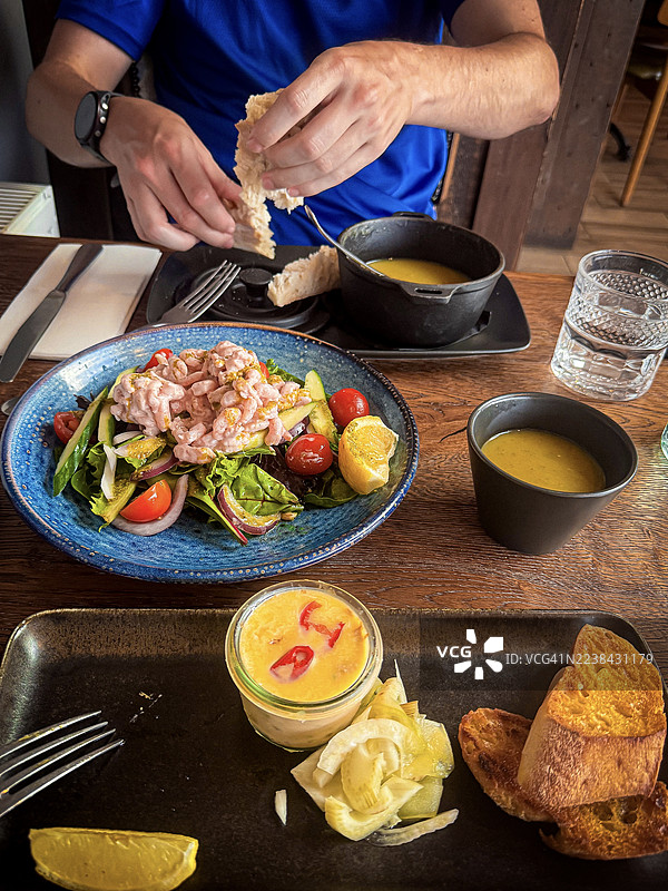 餐厅餐桌上，一个男人正在享用沙拉、汤和面包的餐点（中景）图片素材