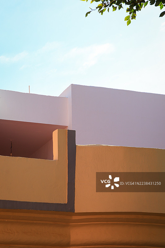 低角度拍摄的建筑，具有几何形状，背景是明亮的蓝天，绿色叶子作为前景，地点：西班牙拉斯帕尔马斯-德格兰卡纳里亚。图片素材