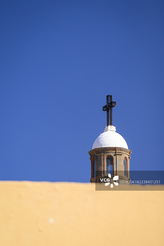 从低角度拍摄的教堂尖塔，顶部有十字架，背景是晴朗的蓝天，前景是黄色的墙壁，地点：西班牙拉斯帕尔马斯-德格兰卡纳里亚图片素材