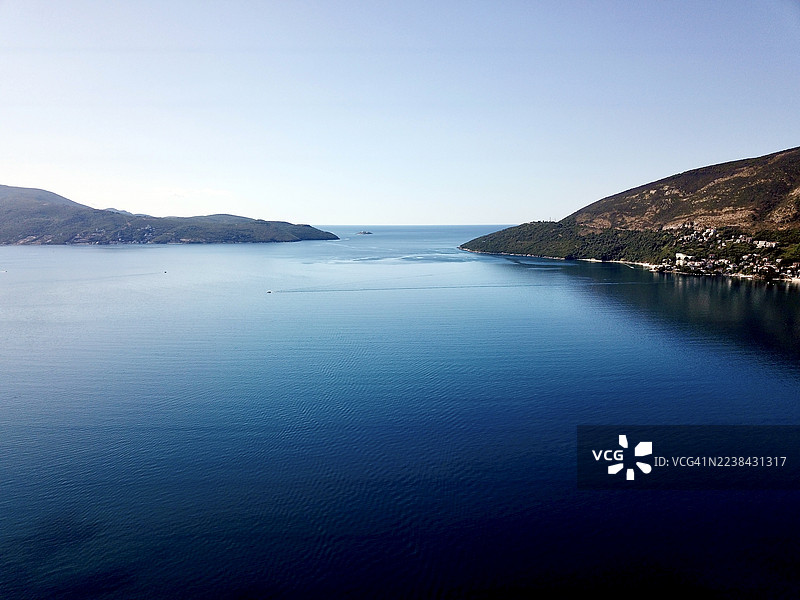 黑山，黑塞格诺维，晴朗天空下，远处群山环绕的清澈蓝色海湾的鸟瞰图，图片素材
