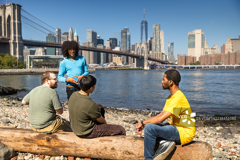 布鲁克林晴朗日子里，四位不同肤色的朋友在鹅卵石海滩边聚会图片素材
