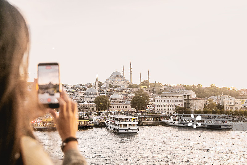 年轻的女游客特写，她正用相机拍摄伊斯坦布尔的全景，背景是清真寺。图片素材
