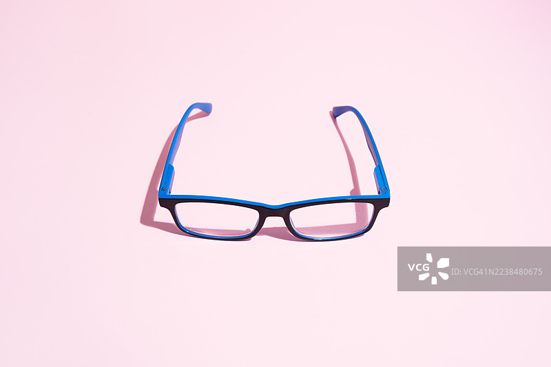 粉色背景上的蓝黑色眼镜投下阴影图片素材