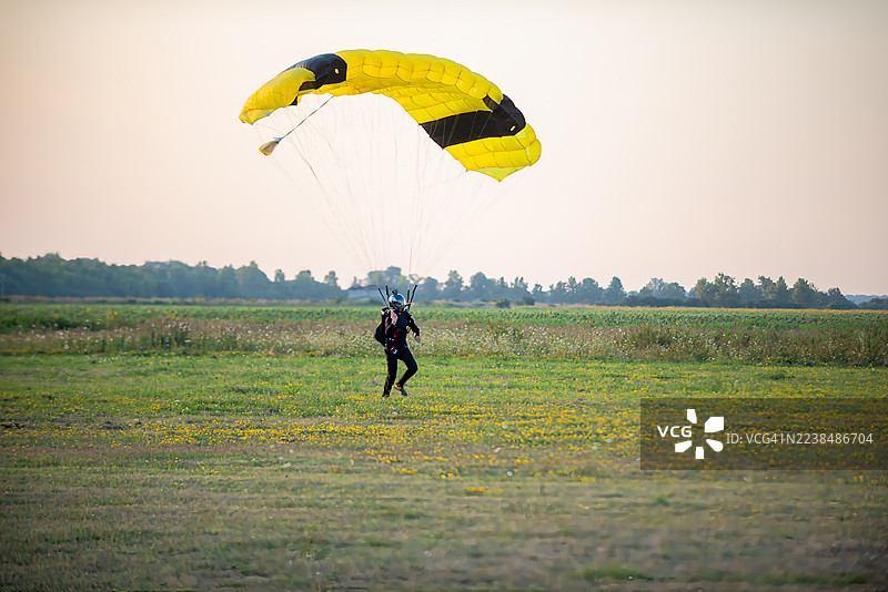 跳伞爱好者在一片绿色的田野上，伴随着鲜黄色的降落伞，轻轻着陆。图片素材
