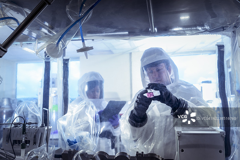 科学家在隔离手套箱中工作，在实验性晶体实验室检查溶液瓶。图片素材